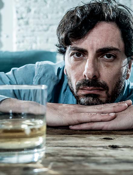 грустный мужчина за столом со стаканом алкоголя