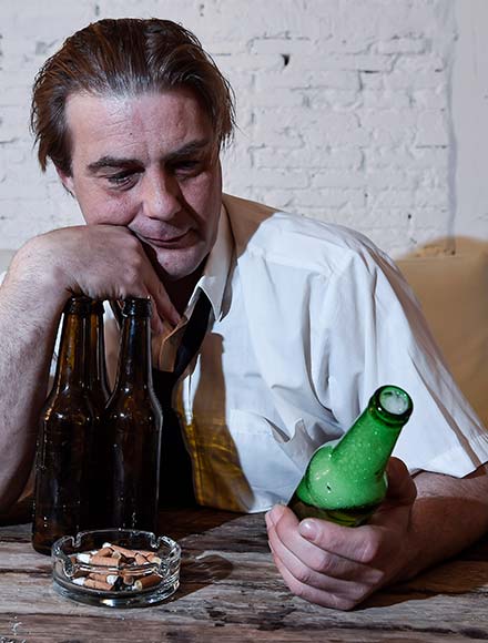 пьяный мужчина сидит за столом и смотрит на бутылку пива